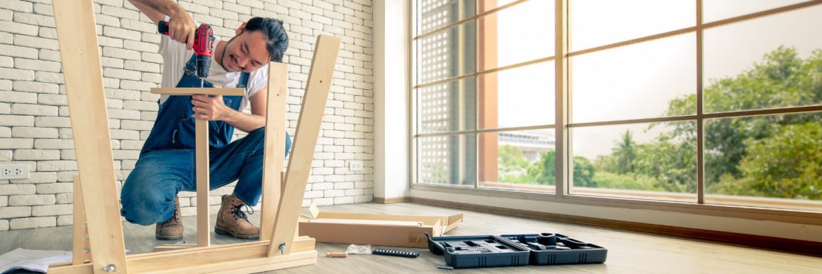 A handyman is working hard on a wooden frame in front of a window.